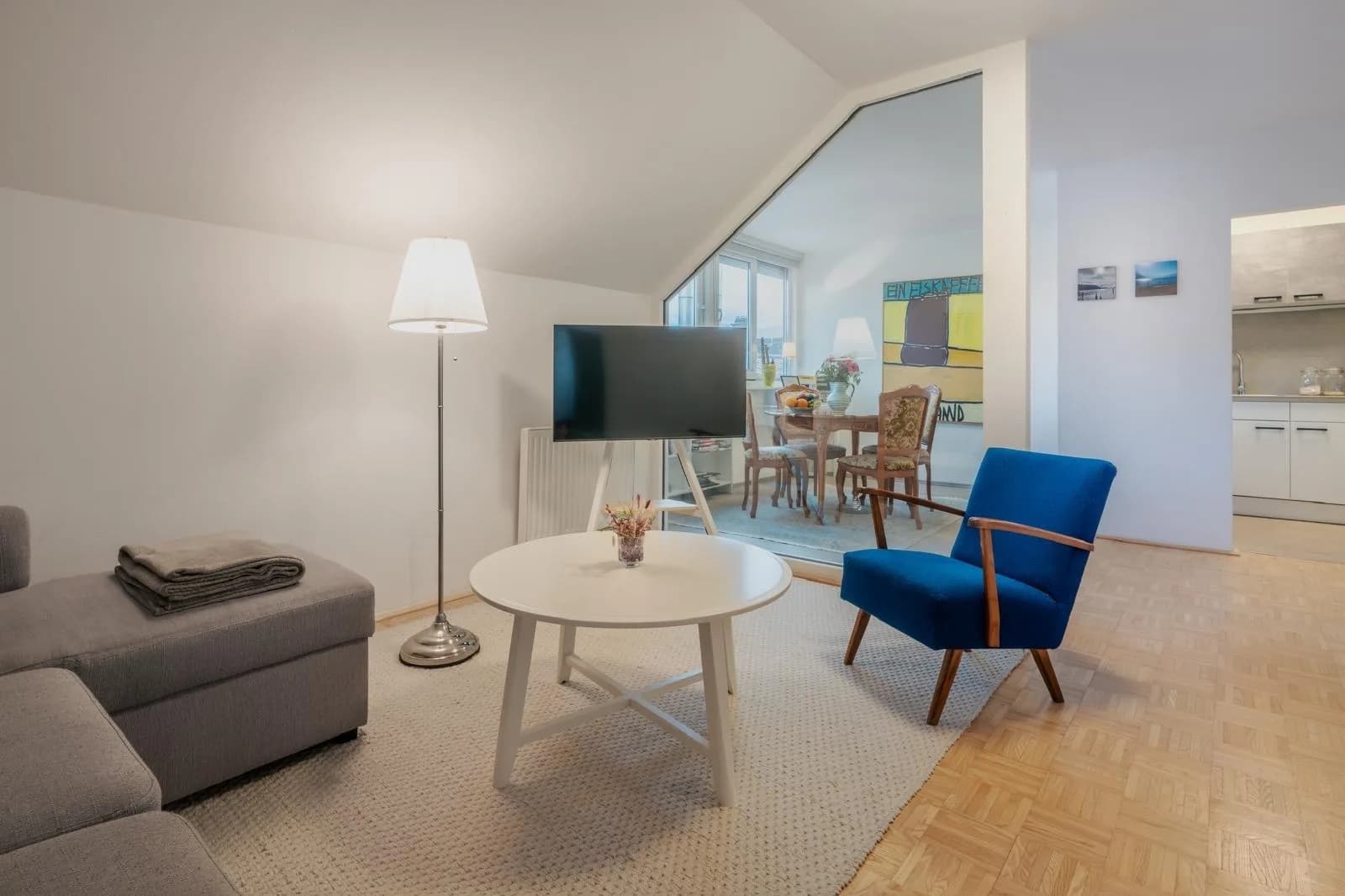 Wohnraum mit Sofa, blauem Sessel, Couchtisch und Fernseher, Blick durch die Glaswand zum Essplatz